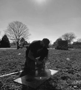 A man outside working with tools in the grass.